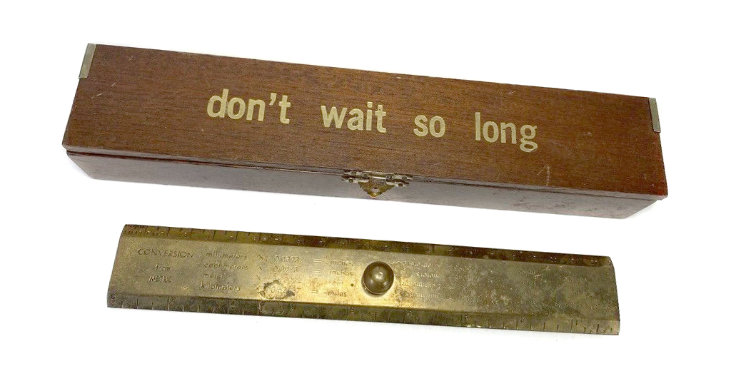 Stained wooden box with "Don't Wait so Long" printed in gold foil on top with a brass conversion ruler.