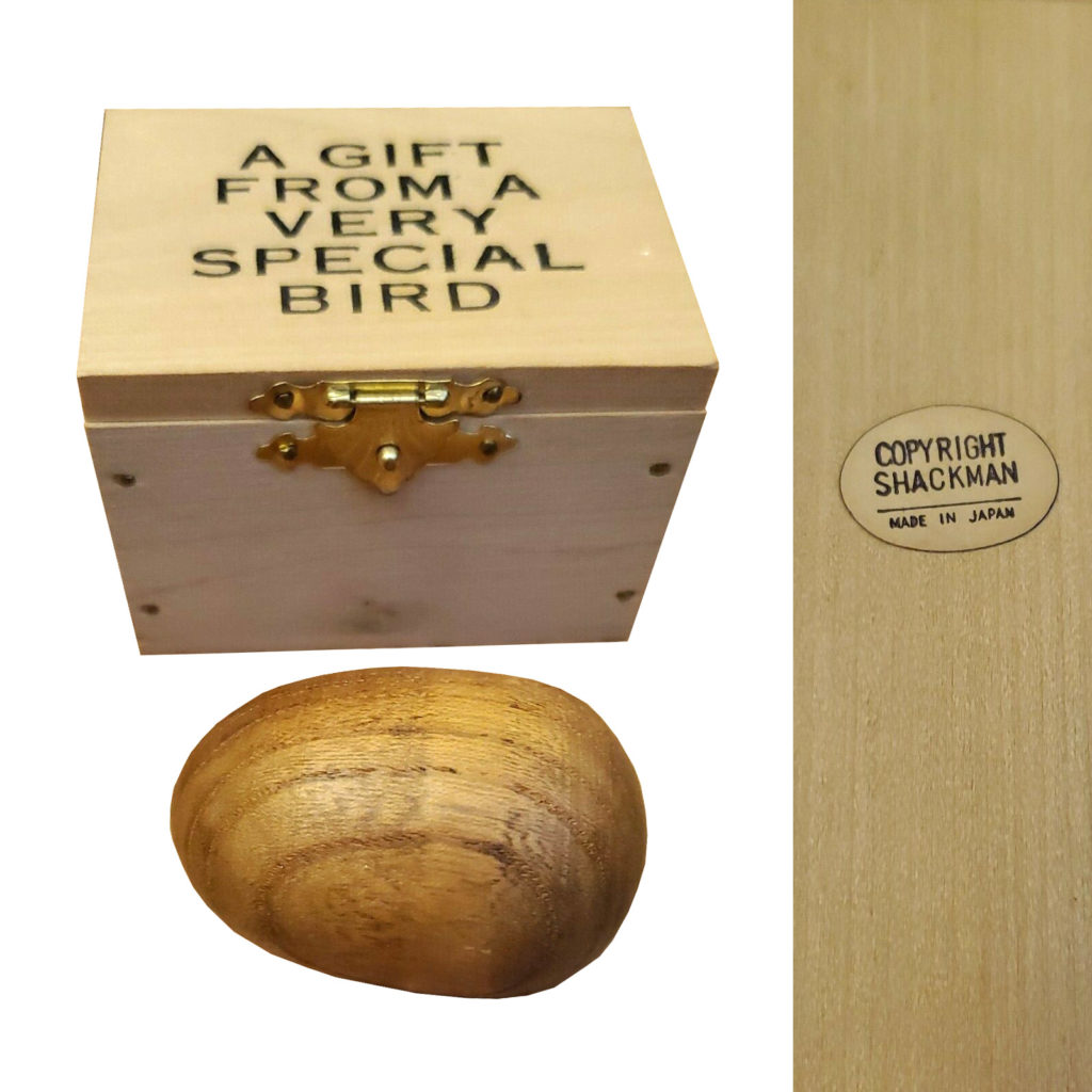 Fake Carl Auböck wooden box with "A gift from a very special bird" printed in black on top and wooden egg shaped paperweight. With a closeup of the oval paper "Copyright Shackman / Made in Japan" sticker.